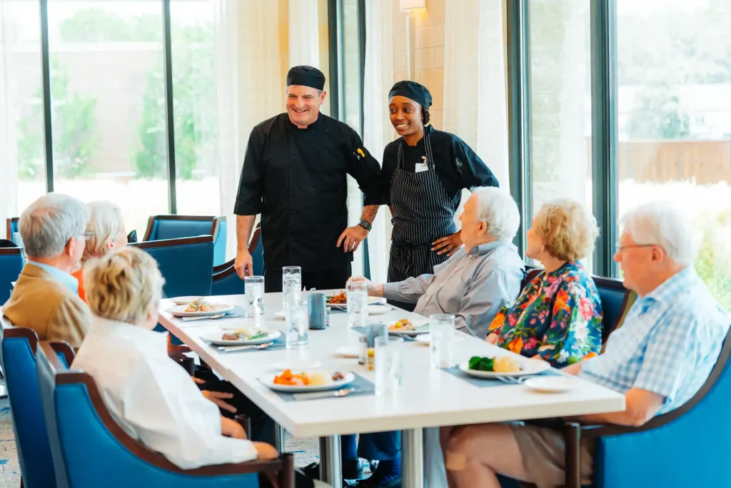 A group of senior adults sit at dinner, speaking to chefs