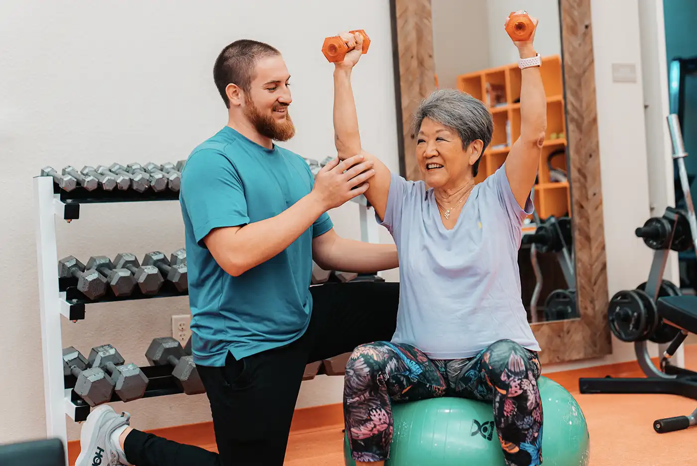 A trainer suggests a posture to a senior woman during a workout in a gym