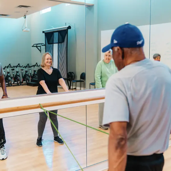 Two senior adults watch their form in a floor-length mirror at a training gym