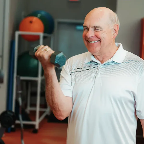 A senior man works with free weights on a gym