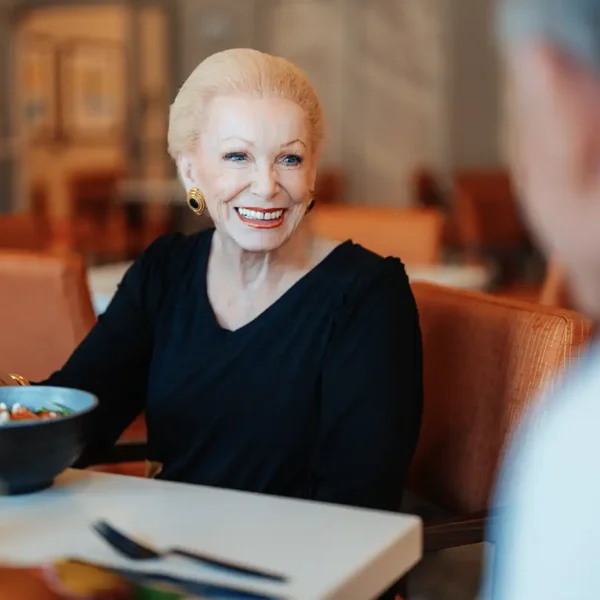 A senior woman smiles across a cafe table at their companion