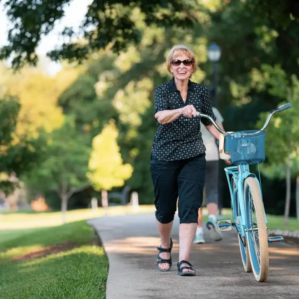 A senior woman walks her bike up a wooded concrete path