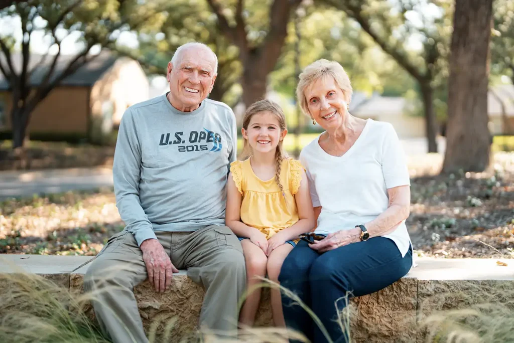 A senior couple sit on an outdoor wall alongside their young great-granddaughter 