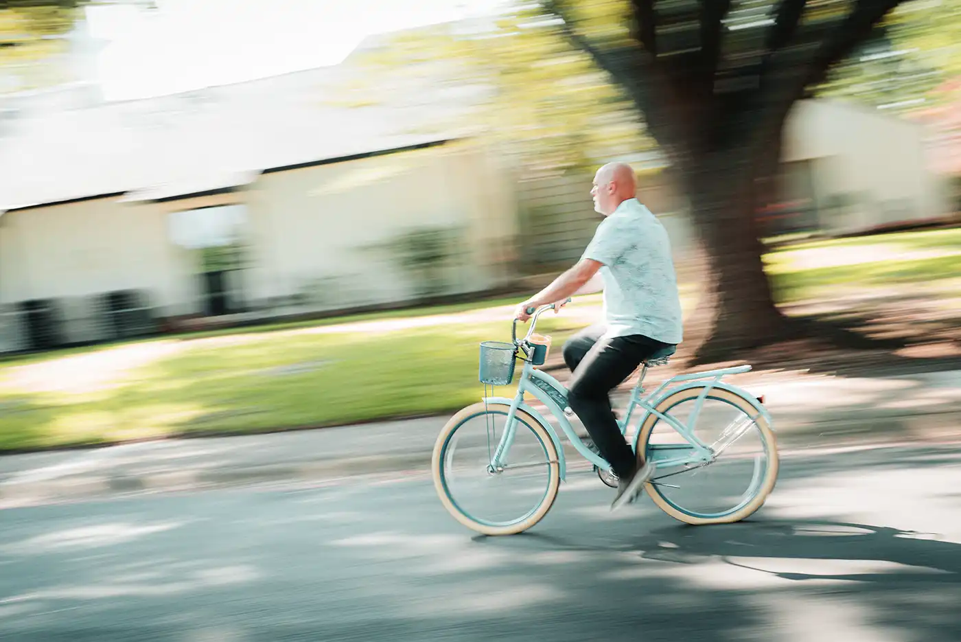 A senior man rides a cruiser-style bicycle down a neighborhood street 