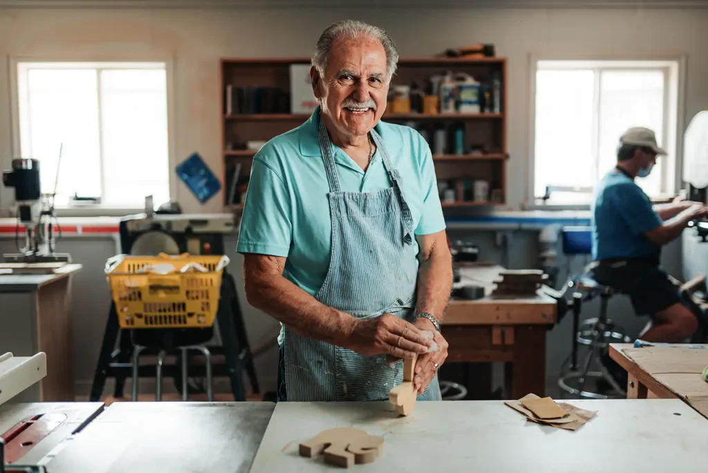 A senior man sands a small wooden object in a workshop