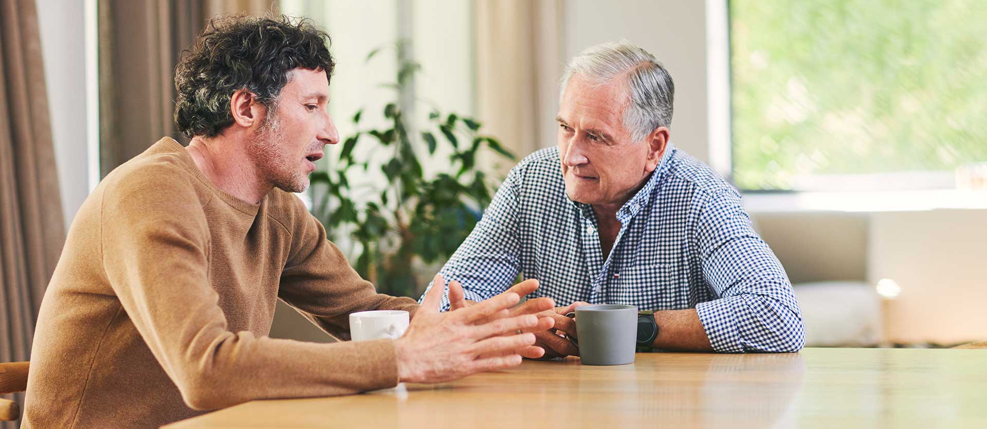 mature man and his elderly father having coffee and a chat at home.